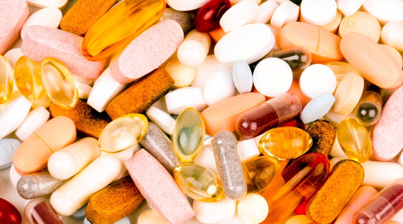 Assorted tablets, capsules and softgels arranged on a white surface.