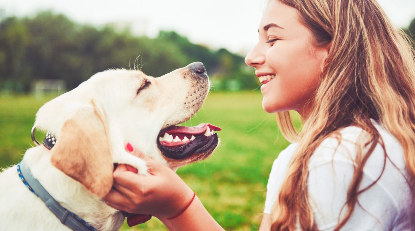 Woman smiling at a Labrador outdoors while holding the dog gently.